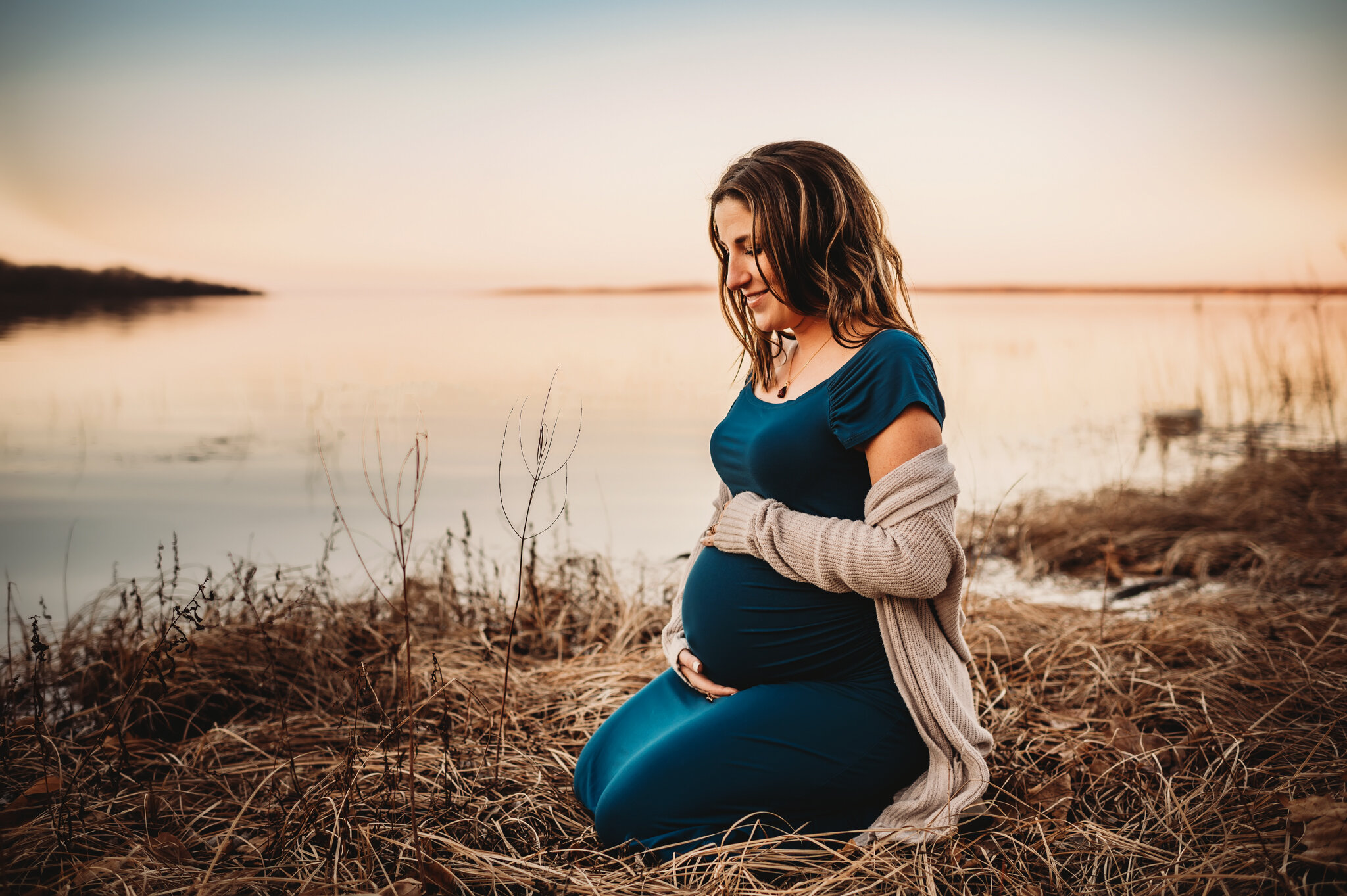 metamora maternity photographer, pregnant mom kneels by river with sunset behind her
