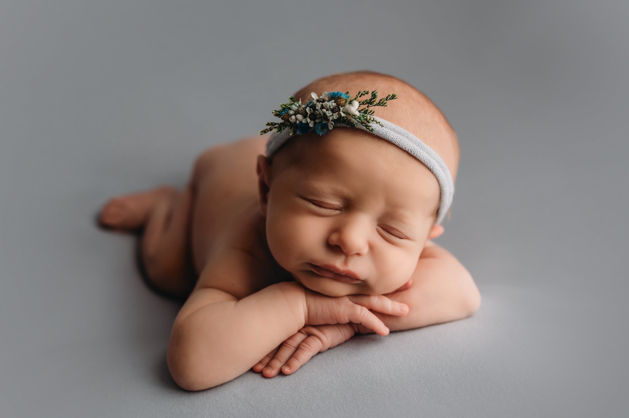 Newborn baby posing on blue with head on hands.jpg