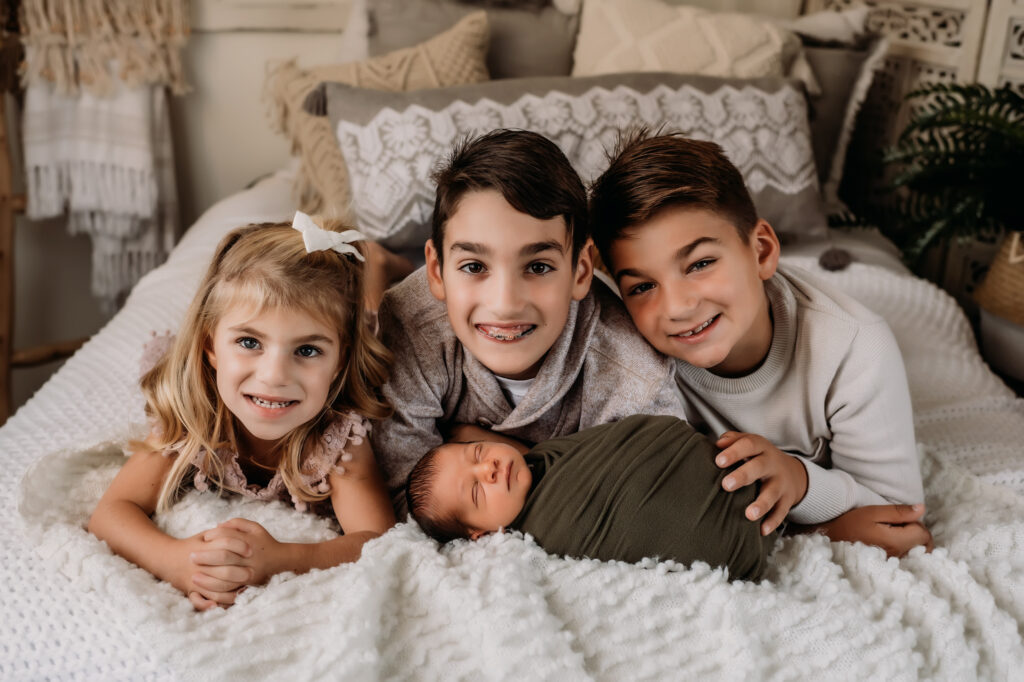 Siblings pose with newborn brother laying on bed