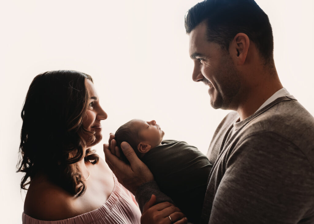 mom and dad smile at each other backlit newborn photo