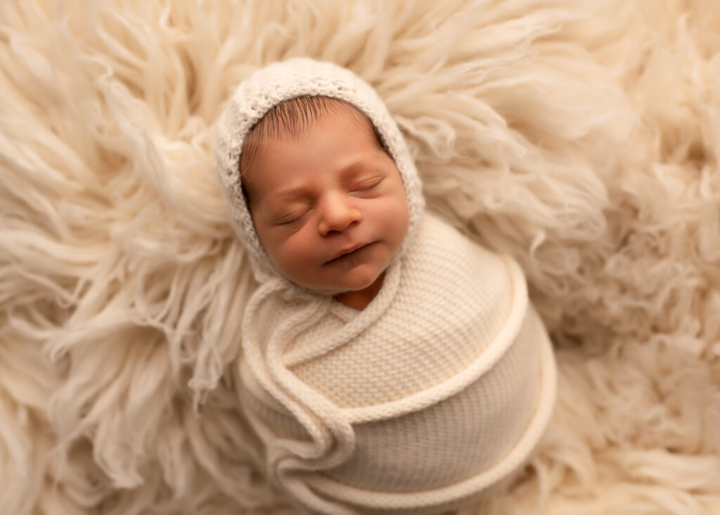 baby lays on cream fur with cream knit bonnet