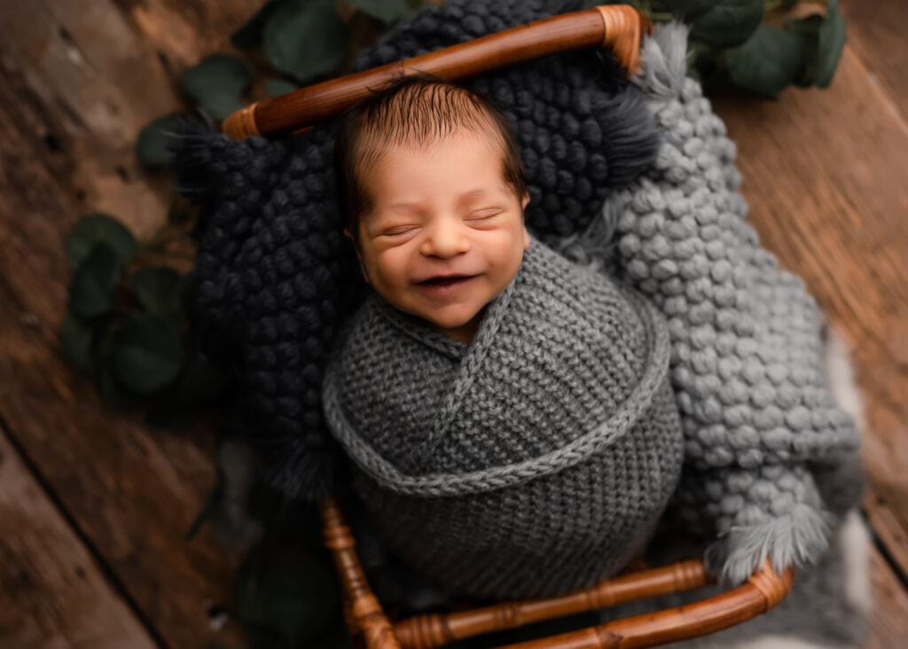 newborn baby boy smiles on bamboo bed in grey wrap