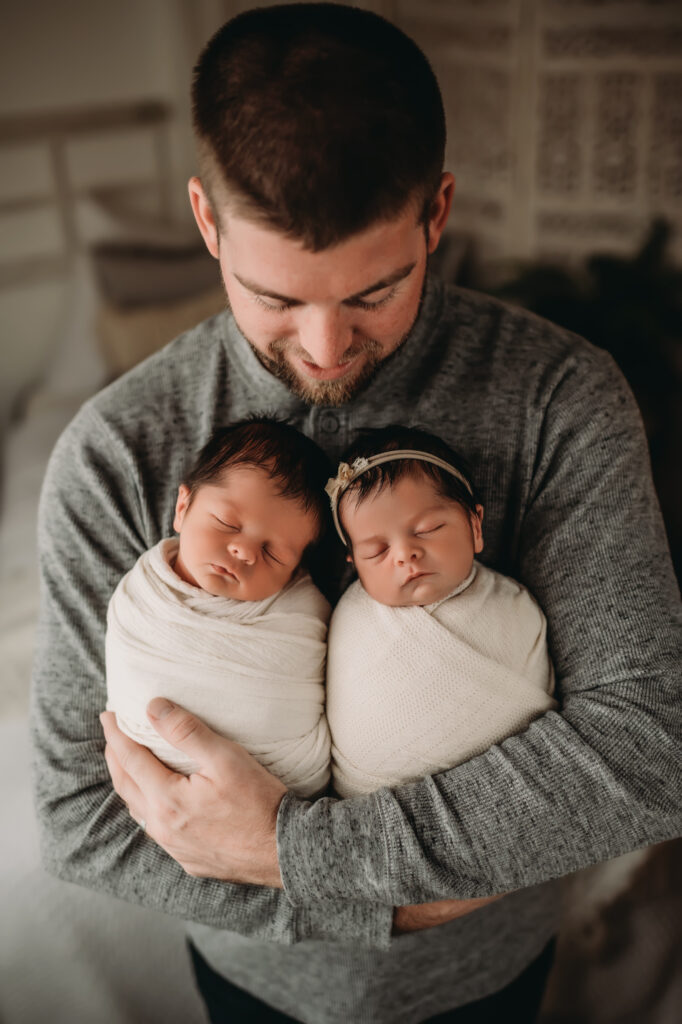 Dad holds boy and girl twins wrapped in cream wraps