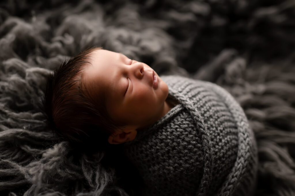 baby boy lays on gray fur in gray knit wrap