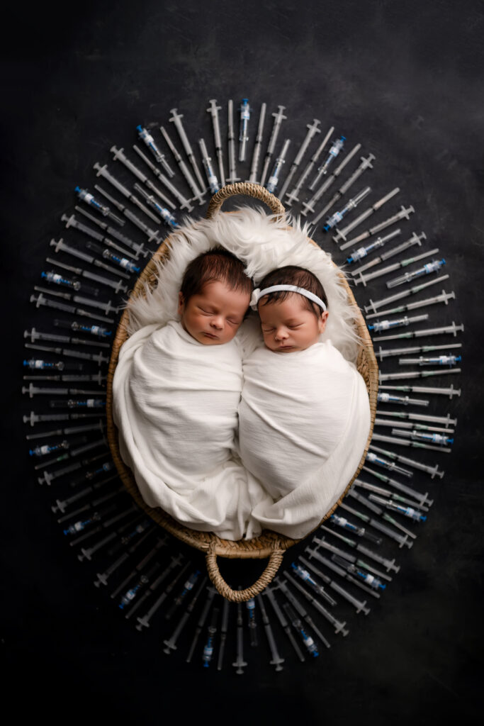 boy and girl twins lay together surrounded by ivf syringes