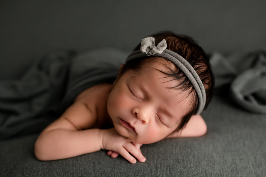 newborn baby girl lays on sage colored fabric with bow in her hair