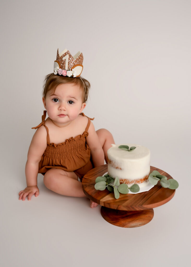 girl sits on white paper behind cake in brown outfit