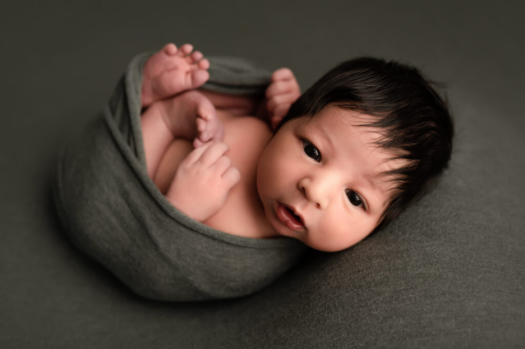 newborn baby has eyes open and is in an olive green wrap. newborn photos in peoria